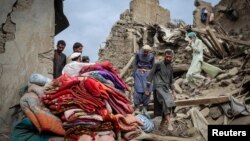 Bărbați afgani merg pe molozul unei case avariate în urma unui cutremur cu magnitudinea de 6 grade pe scara Richter care a lovit estul Afganistanului.