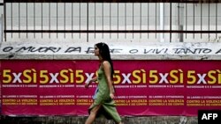 Një grua duke ecur përskaj postarëve të fushatës që bën thirrje për të votuar në referendum.
