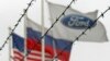 (Left to right:) The flags of the United States, Rusia and the Ford motor company fly behind barbed wire at an automobile plant in Vsevolozhsk. The automobile plant announced this week that it is closing three of its factories in Russia. (file photo)