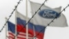 (Left to right:) The flags of the United States, Rusia and the Ford motor company fly behind barbed wire at an automobile plant in Vsevolozhsk. The automobile plant announced this week that it is closing three of its factories in Russia. (file photo)