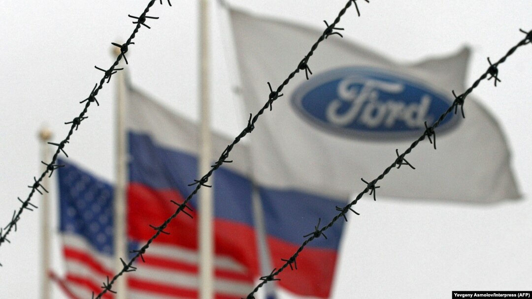 (Left to right:) The flags of the United States, Rusia and the Ford motor company fly behind barbed wire at an automobile plant in Vsevolozhsk. The automobile plant announced this week that it is closing three of its factories in Russia. (file photo)