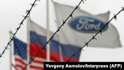 (Left to right:) The flags of the United States, Rusia and the Ford motor company fly behind barbed wire at an automobile plant in Vsevolozhsk. The automobile plant announced this week that it is closing three of its factories in Russia. (file photo)