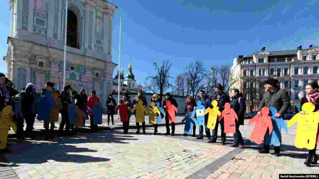 Активісти тримають у руках картонні людські фігури на пам&#39;ять про Решата Аметова, кримськотатарські прапорці; деякі активісти тримали маленькі паперові фігури із заклеєним ротом, символізуючи порушення прав людини в анексованому Росією Криму