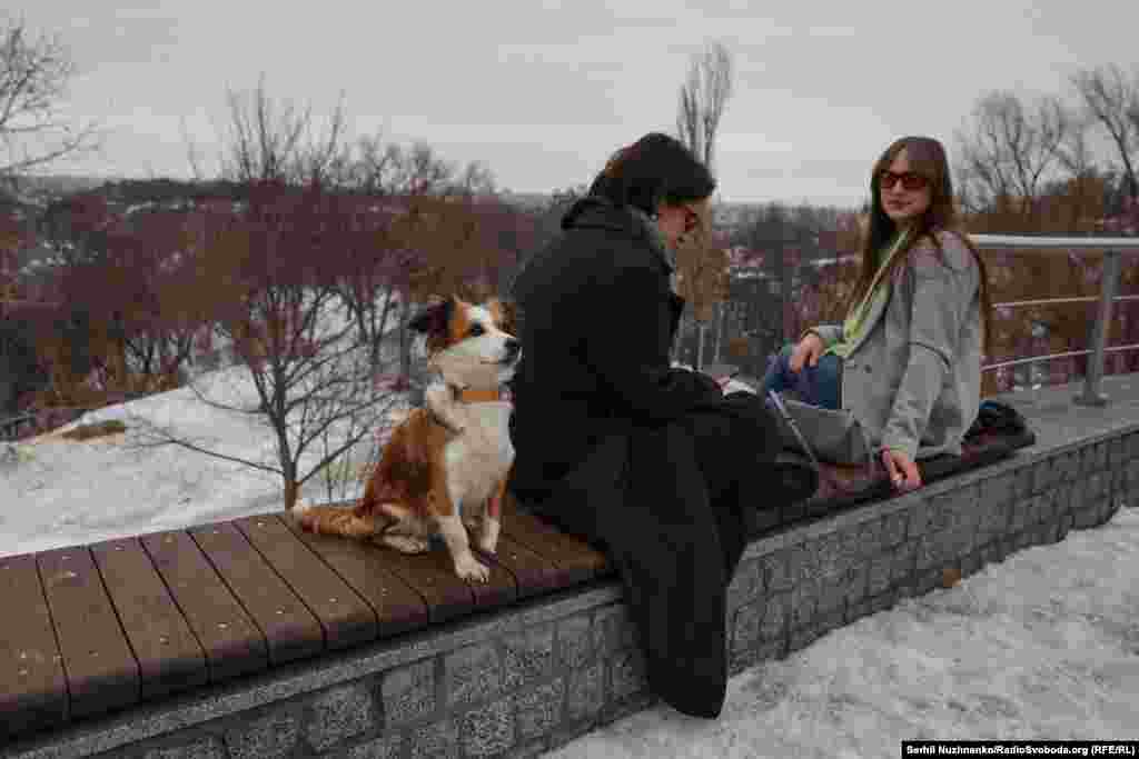 Двоє дівчат пʼють каву, біля них сидить собака.Таня (ліворуч): «Я зустріла вдома. І перше, що я почула – це дзвінок мого телефону серед ночі. Я прокинулась, мені дзвонив друг, каже: «Він напав». Кажу: «Хто напав?» Каже: «Путін». А потім я почала дзвонити всім своїм рідним».Шеріл (праворуч): «Я російське вторгнення зустріла в гуртожитку. Мене розбудила подруга, сказала, що почалася війна. Я допомагала їй зібратись. Сама потім лягла спати».У маленької собаки, яка бавиться біля дівчат, відсутня частина передньої лапи. Звати її Любушка, їй два роки. Любушка зустріла війну у Мирнограді. Її власниця Таня допомагала з евакуацією тварин з Донеччини, будувала вольєри в притулку біля Києва, а потім забрала Любушку до себе