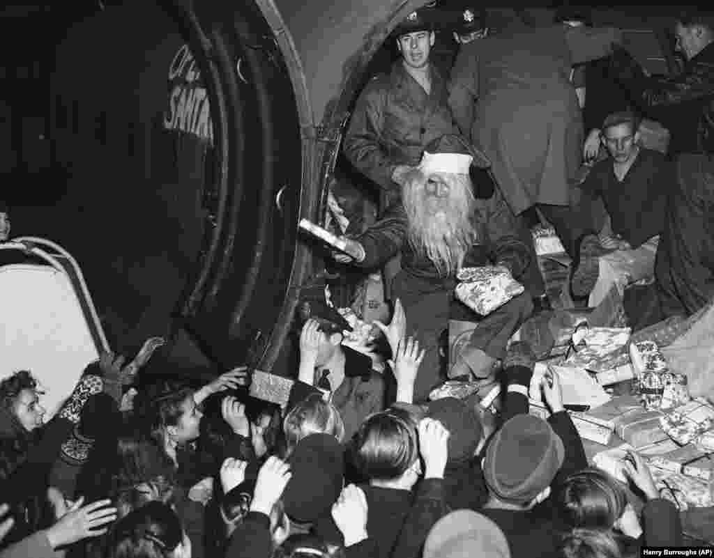 Copii berlinezi pe aeroportul Tempelhof din Berlin la 15 decembrie 1948 primind cadouri de Crăciun de la un pilot Moș Gerilă, cunoscut ca locotenentul John Konop din Astoria, New York. Evenimentul s-a petrecut la sosirea primului avion cu daruri din partea donatorilor americani, distribuite în cadrul programului Forțelor Aeriene americane cunoscut ca &bdquo;Operațiunea Santa Claus&rdquo;.