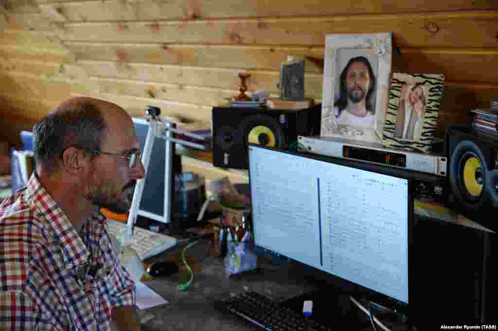 Violinist and Vissarion follower Dimitr Khemetov works in front of a portrait of Vissarion. Most inhabitants of the settlement were brought up in the Soviet Union, where Christianity was repressed. Many early converts to Vissarion's cult had little understanding of religion. 
