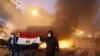 Masked Egyptian demonstrators hold the national flag as they stand next to a burning police vehicle in Cairo.