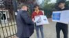 Қазақстанның Амстердамдағы елшілігі алдында наразылық өткізіп тұрған Қымбат Әбеуұлы (ортада) және Тасқын Құдайберген елшілік өкілімен сөйлесіп тұр. 25 тамыз 2025 жыл. Скриншот 