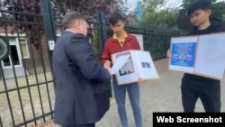 Қазақстанның Амстердамдағы елшілігі алдында наразылық өткізіп тұрған Қымбат Әбеуұлы (ортада) және Тасқын Құдайберген елшілік өкілімен сөйлесіп тұр. 25 тамыз 2025 жыл. Скриншот