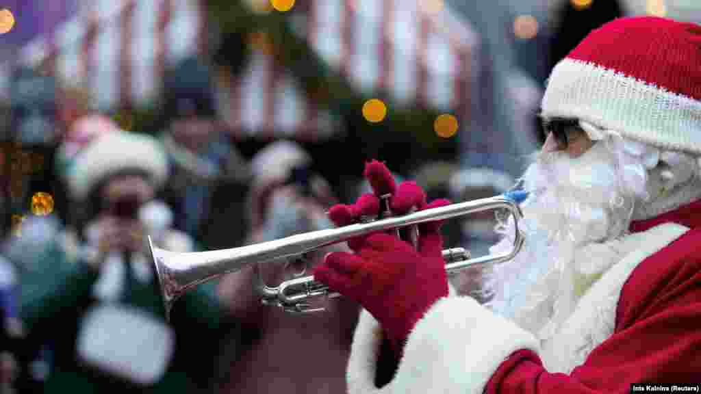 Čovjek u kostimu Deda Mraza trubi u rog prije dobrotvorne akcije Santa Fun Run u Rigi, Latvija, 8. decembra 2024.