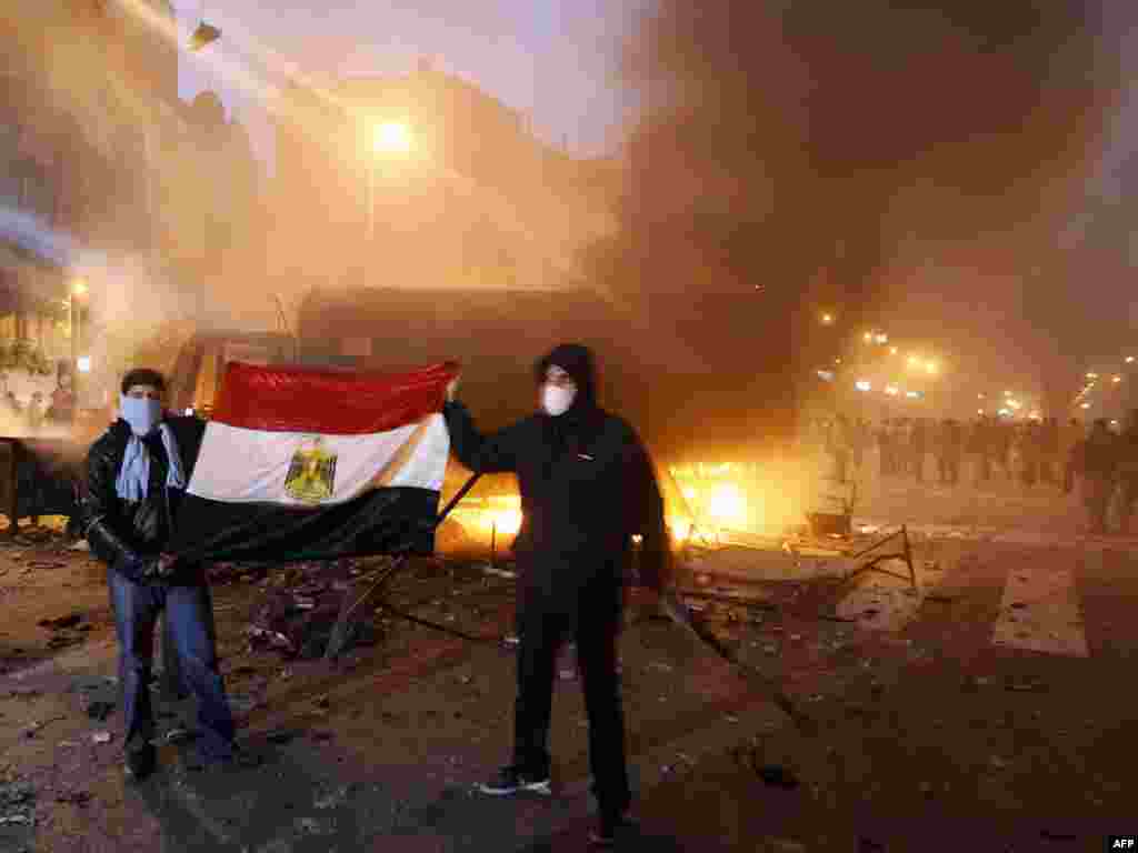 Masked Egyptian demonstrators hold the national flag as they stand next to a burning police vehicle in Cairo.