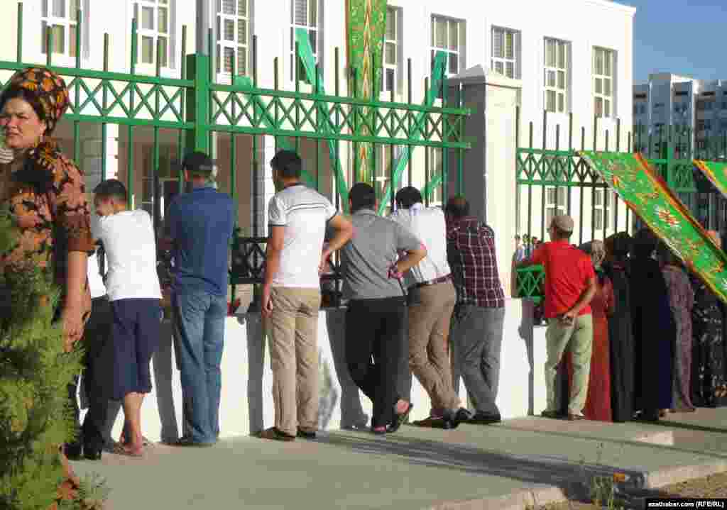 Aşgabatda mekdep baýramçylygy. Çärä tomaşa edip bilmedikler derwezenäniň daşyndan seredýärler.