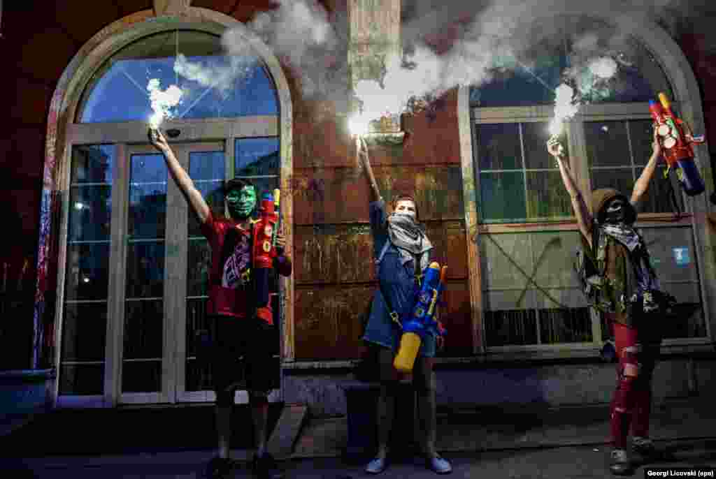 Protestuesit mbajnë fishekzjarrë pas ngjyrosjes së fasadës së Ministrisë së Drejtësisë në kryeqytetin e Maqedonisë, Shkup, më 31 maj. Pjesëmarrësit në protestat e vazhdueshme antiqeveritare e kanë quajtur këtë lëvizje &ldquo;Revolucioni shumëngjyrësh&rdquo;. (epa/Georgi Licovski) &nbsp;