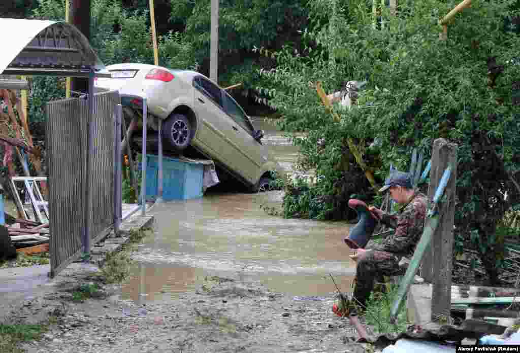 Un bărbat își golește cizma de cauciuc de apă în timp ce stă lângă o mașină avariată de ploile puternice care au&nbsp;provocat&nbsp;inundații și în&nbsp;așezarea&nbsp;Kuibysheve, lângă&nbsp;Bakhchisaray, pe 4 iulie.&nbsp;