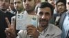 Iran -- Iranian President Mahmud Ahmadinejad flashes the victory sign with an ink-stained finger as he holds up his identity cards at a polling station in Tehran, 12Jun2009