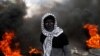 A Palestinian demonstrator stands near burning tires during clashes with Israeli troops.
