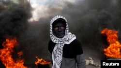 A Palestinian demonstrator stands near burning tires during clashes with Israeli troops.