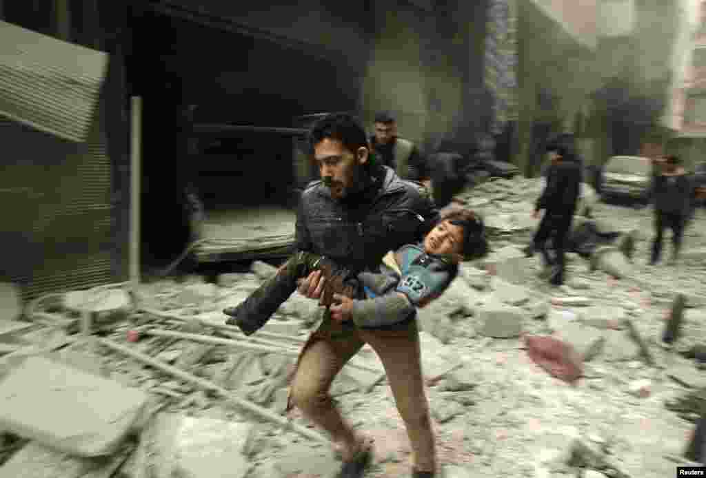 Një burrë mban një fëmijë në krah gjatë ikjes nga sulmet ajrore të forcave qeveritare në Aleppo të Sirisë, më 21 janar. (Ammar Abdullah, Reuters)