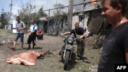 Local residents pass the covered body of an apparent civilian casualty in the village of Stanitsa Luhanskaya, in the eastern industrial province of Luhansk, on July 2.
