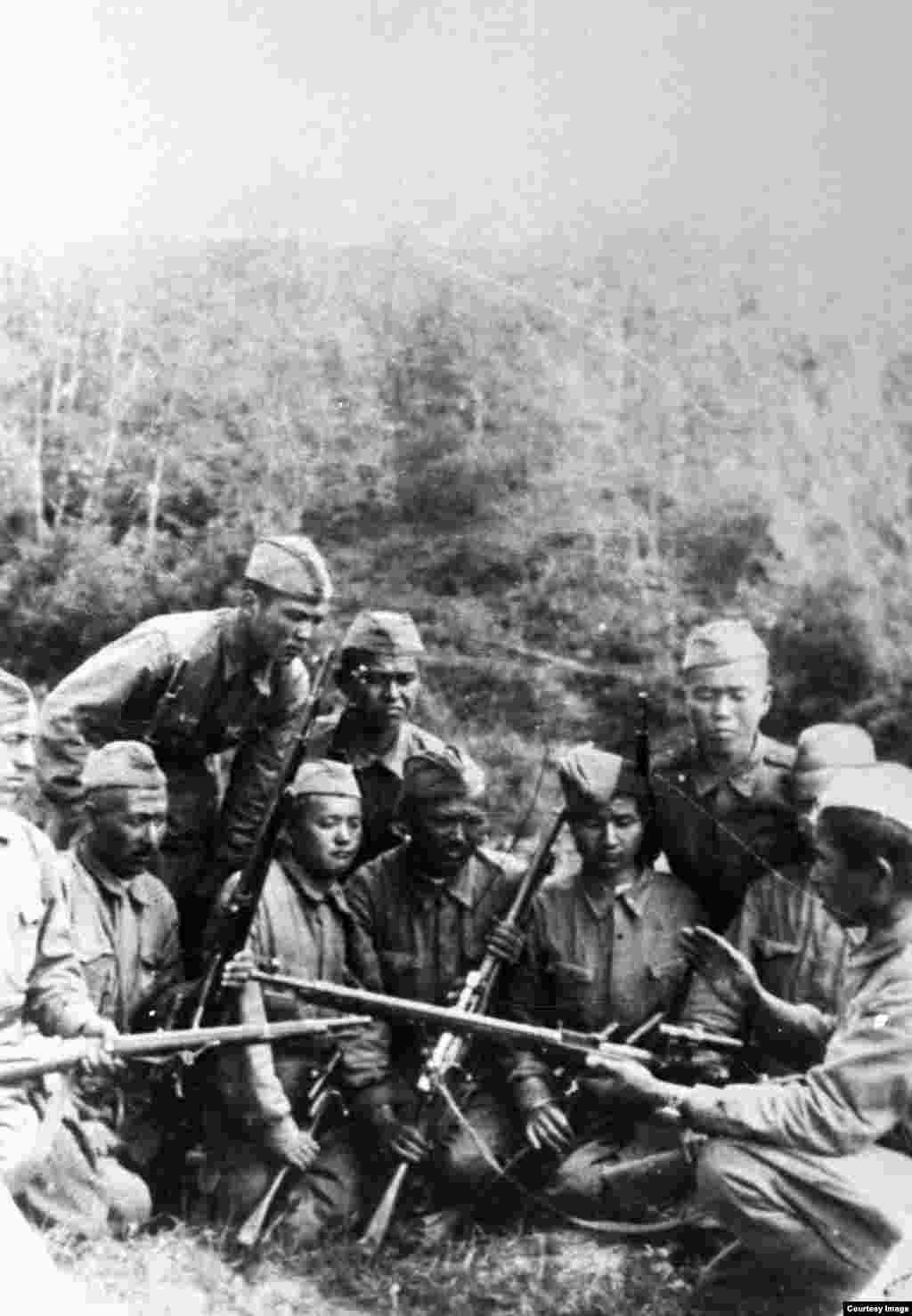 Архивте бұл фотографияға "К. Ұлыбаев - мерген (оң жақта) майдандастарының арасында. 1944 жыл" деген сипаттама жазылған.
