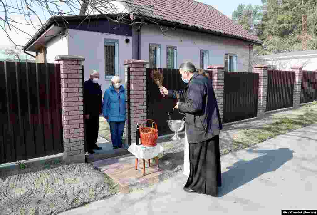 Православен свештеник благословува велигденски колачи и јајца додека одржува растојание од една постара двојка во село во близина на Киев на 19 април.