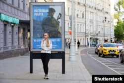 Дівчина стоїть біля плаката у Москві із закликом на військову службу за контрактом в російській армії