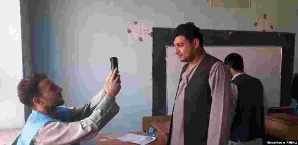 کارمند کمیسیون مستقل انتخابات افغانستان در حال گرفتن عکس یک رأی دهنده توسط دستگاه بیومتریک در یکی از مراکز رأی دهی در ولایت فاریاب.