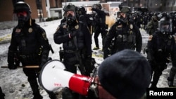 Демонстрант с мегафон пред полицейски служители, които охраняват хотел в Мейпъл Гроув, Минесота, където се предполага, че е отседнал Грег Бовино, отстранен от поста си на началник на граничната патрулна служба