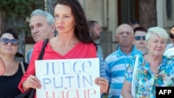 Boeing 777 ұшағы жолаушыларының қазасына қатысты Харьковтегі қаралы жиынға келген әйел "Путин Гаага сотына тартылсын" деген плакат ұстап тұр.