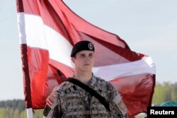 Латвийский солдат держит национальный флаг в ожидании прибытия около 150 американских десантников 173-й пехотной бригады армии США, базирующейся в Италии. Аэропорт Риги, 24 апреля 2014 года, фото Reuters