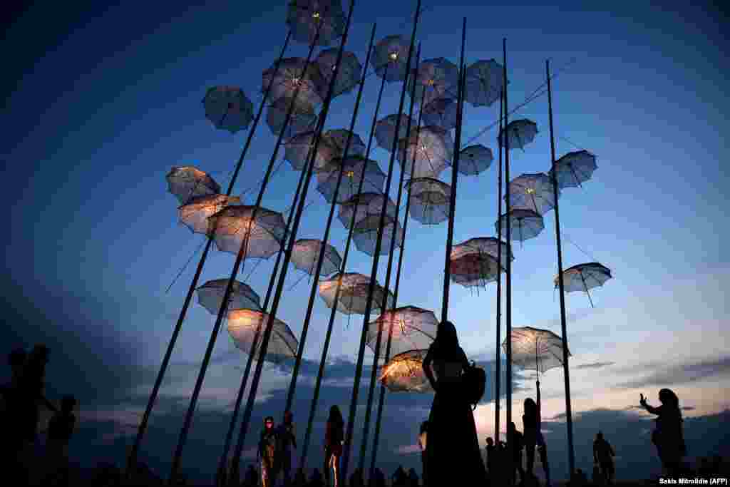 People take photos under the &quot;Umbrellas&quot; sculpture by Greek sculptor George Zongolopoulos on the new waterfront in Thessaloniki. (AFP/Sakis Mitrolidis)