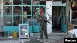 Afghan National Army (ANA) soldiers stand guard in front of a shop burned during the Taliban attack on Kandahar Airport in Kandahar on December 9.