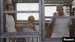 Al-Jazeera journalists (left to right)) Baher Mohamed, Peter Greste, and Mohamed Fahmy stand behind bars in a court in Cairo in June 2014.