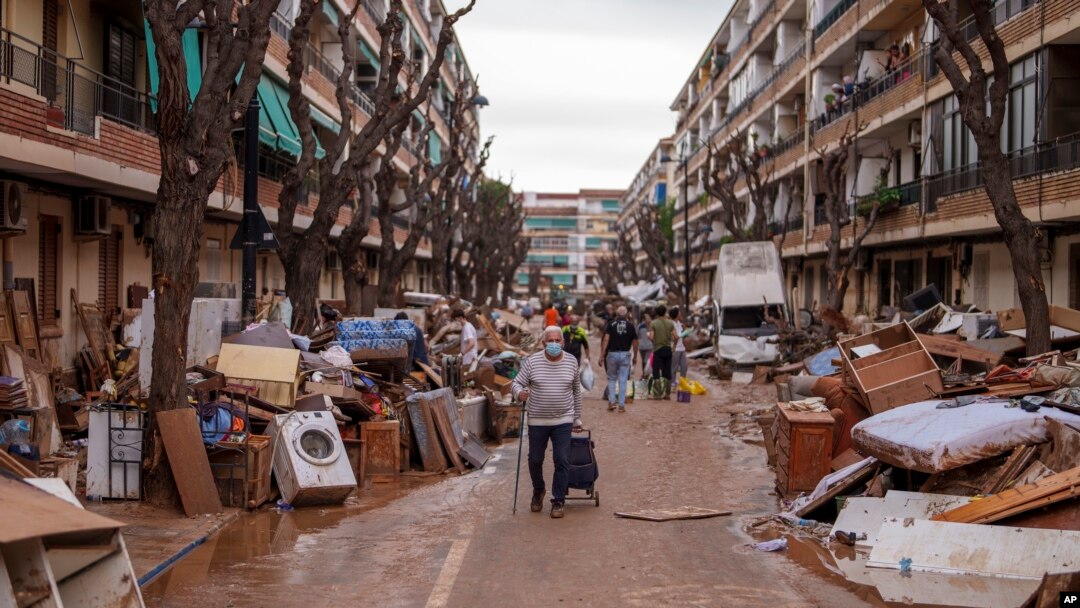 Oamenii trec pe o stradă pe marginea căreia sunt îngrămădite bucăți de mobilier și gunoaie în municipalitatea Benetusser, la sud de Valencia, Spania, 4 noiembrie 2024.