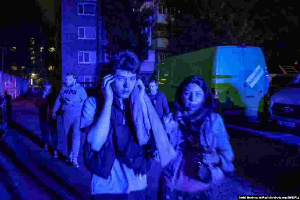 Підліток закриває вуха від звуку дрона, що стрімко йде на зниження для удару неподалік від людей, які біжать в укриття. Київ, 24 травня 2025 року