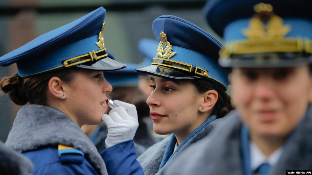 O femeie din Armata Română aplică ruj pe buzele unei colege înainte de parada militară de Ziua Națională a României din București, 1 decembrie 2017.