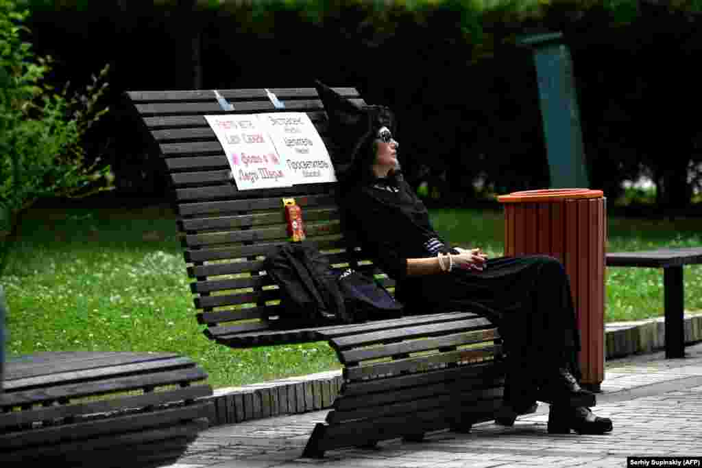 A woman dressed as a witch dozes in the absence of clients as she sits on a bench with a placard reading &quot;Photo with Lady Charm. Psychic. Healer. Educator&quot; in the center of the Ukrainian capital, Kyiv. (AFP/Sergei Supinsky)