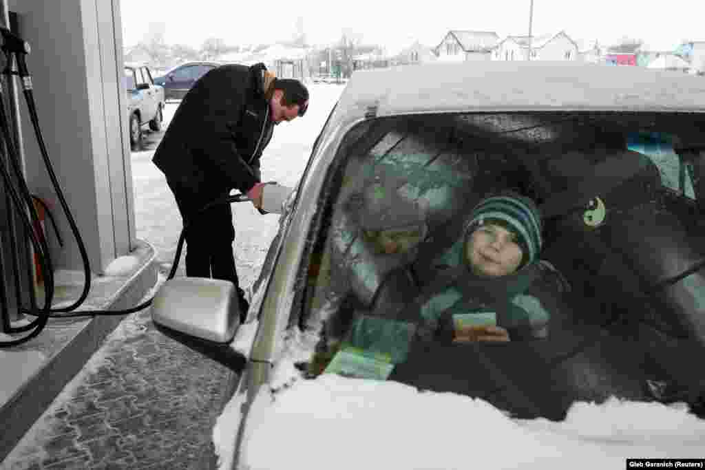 Rozumiy gases up his car as his children wait.