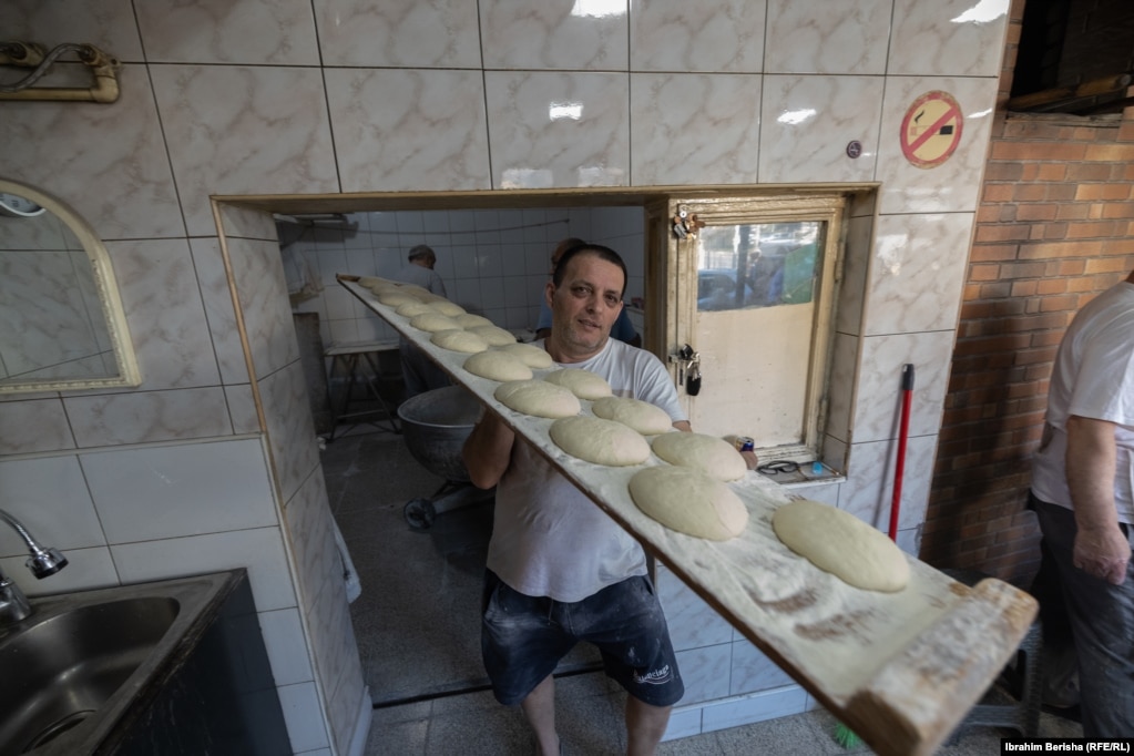 Një punëtor duke i bartur kuleçet e pitalkës në një dërrasë të gjatë para se ato të futen në furrë për pjekje.