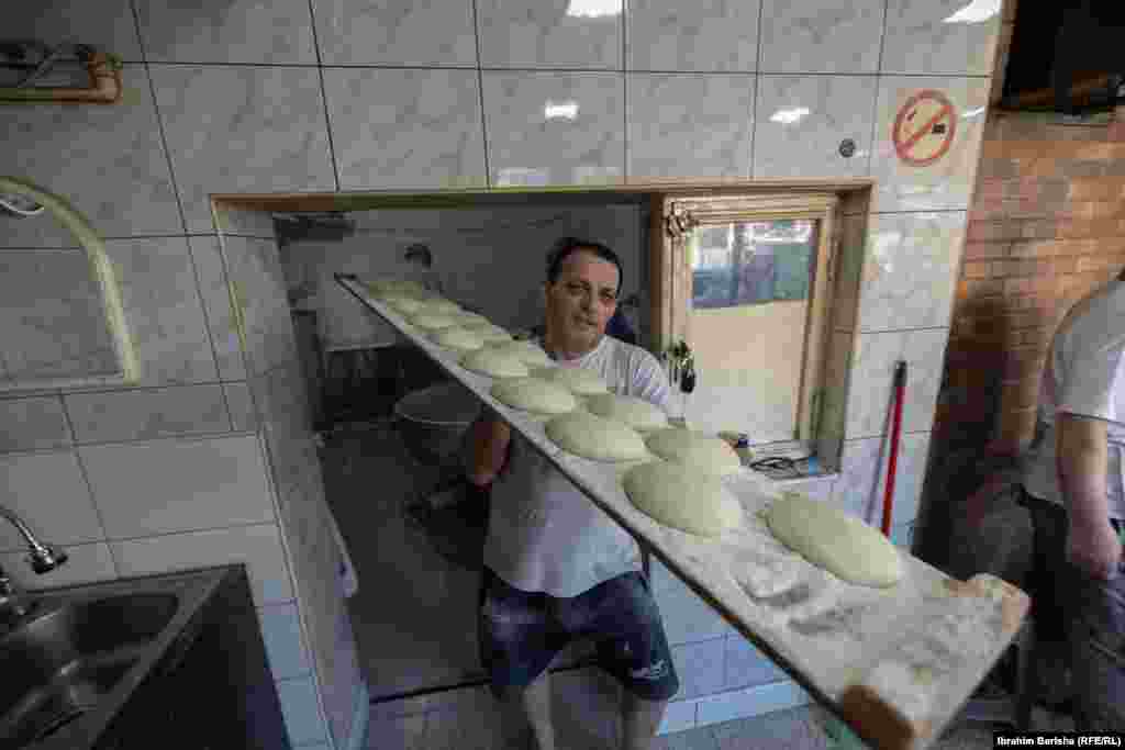 Një punëtor duke i bartur kuleçet e pitalkës në një dërrasë të gjatë para se ato të futen në furrë për pjekje.