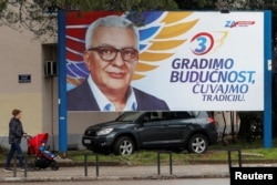 A woman pushes a child in a stroller past a preelection billboard of candidate Andrija Mandic in Podgorica on March 15.