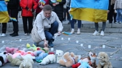 Жена поставя свещ до детски играчки в памет на децата, загинали във войната в Украйна, Пловдив, 24 февруари 2026 г.