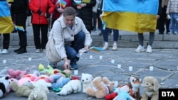 Жена поставя свещ до детски играчки в памет на децата, загинали във войната в Украйна, Пловдив, 24 февруари 2026 г.