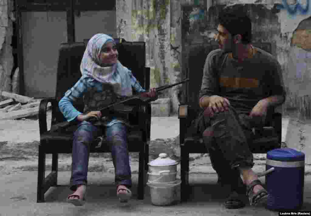 A girl holds a gun across her lap as she sits with a Free Syrian Army fighter on a street in Aleppo. (Reuters/Loubna Mrie)