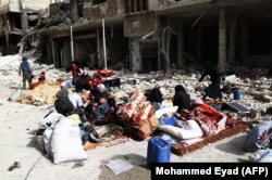 Syrians sit in the street with their belongings as they wait to be evacuated from Arbin in eastern Ghouta on March 27.