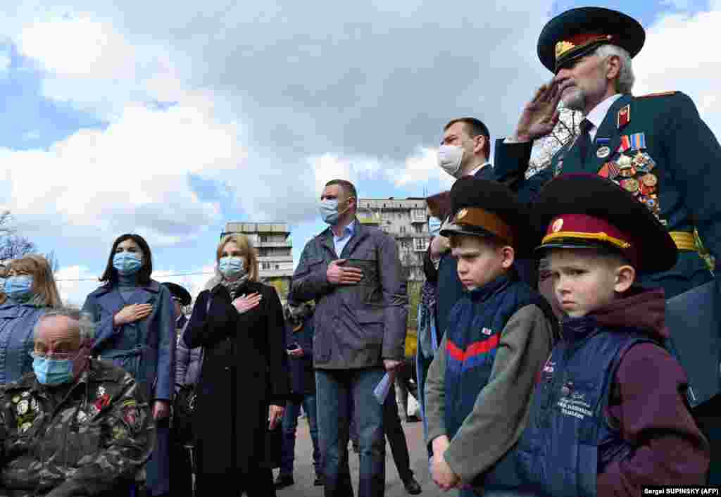 Amid the COVID-19 pandemic, people wear protective face masks as they stand at the Chernobyl memorial in Kyiv on April 26.