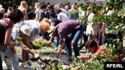 Oamenii plantează flori în timp ce participă la o ceremonie de deschidere a unei grădini publice în memoria Annei