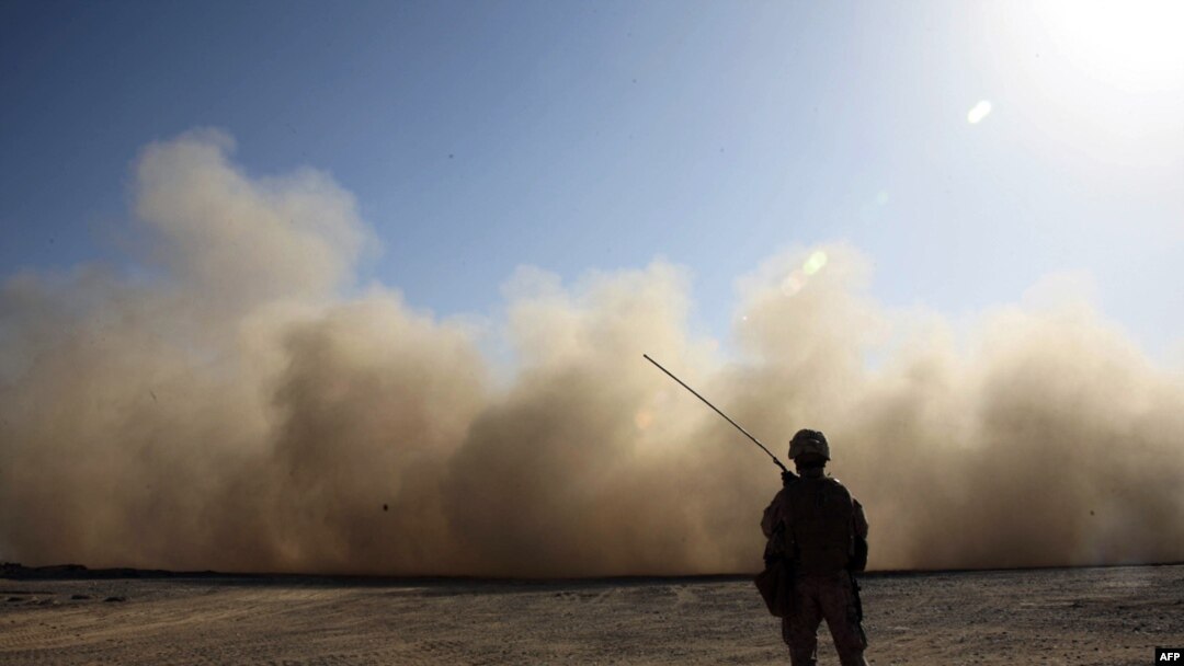 A U.S. Marine stands guard as a landing helicopter churns up a cloud of dust in Marjah, Helmand Province.
