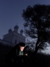 RUSSIA -- A photographer uses his mobile phone near The Church of the Kazan Icon of the Mother of God in the morning mist at dawn in the village of Osenevo, Yaroslavl region, October 6, 2024.