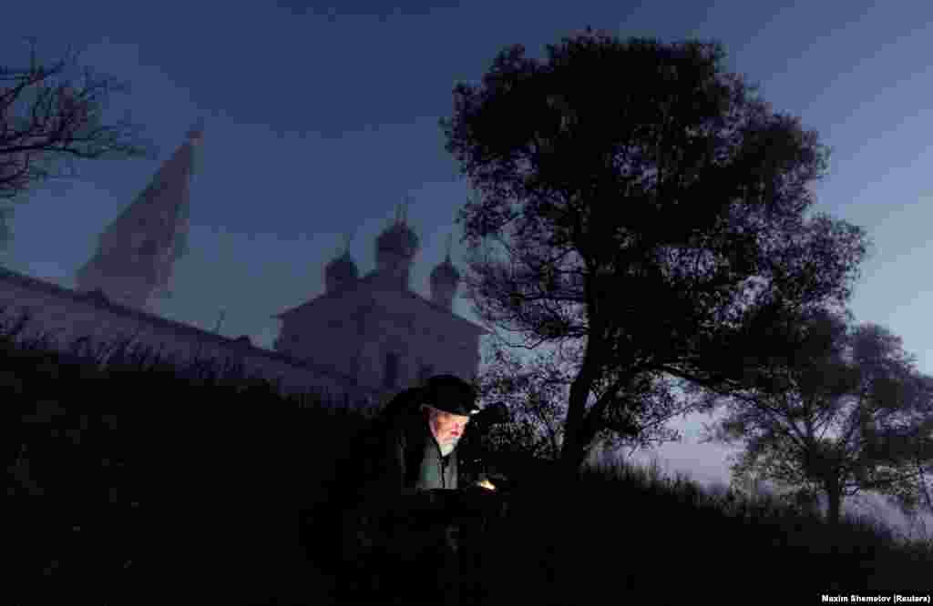 A man uses his mobile phone near the Church of the Kazan Icon of the Mother of God in the morning mist at dawn in the village of Osenevo in Russia&#39;s Yaroslavl region.